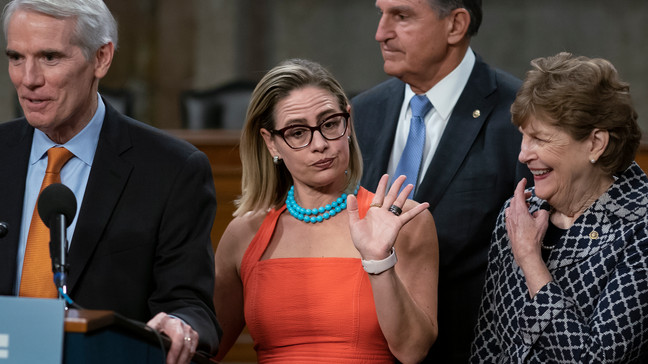 FILE- Sen. Kyrsten Sinema, D-Ariz., center, gestures during a news conference at the Capitol in Washington, Wednesday, July 28, 2021, while working on a bipartisan infrastructure bill with, from left, Sen. Rob Portman, R-Ohio, Sen. Joe Manchin, D-W.Va., and Sen. Jeanne Shaheen, D-N.H. (AP Photo/J. Scott Applewhite, File)